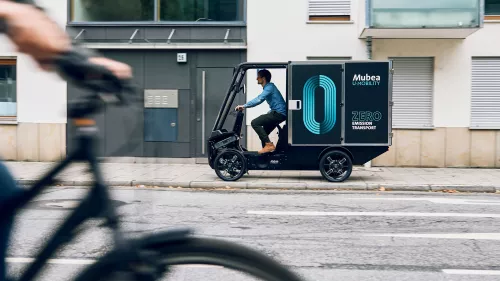 Cargo PACK drives onto the pavement in front of a modern residential building and delivers parcels.